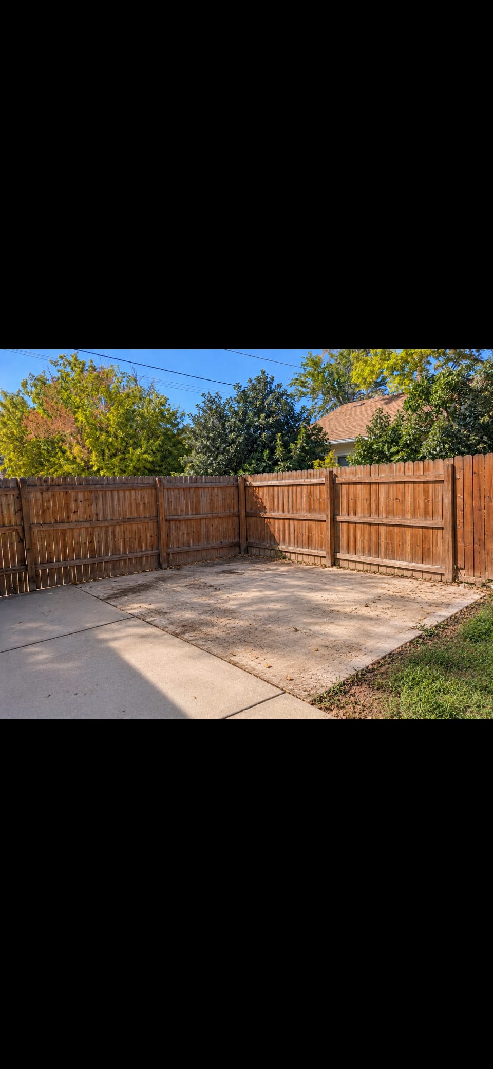 Cleared concrete pad in a fenced backyard after shed demolition and debris removal